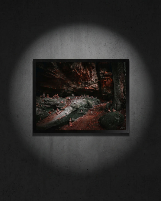 Die Steinstadt – Gerahmter Kunstdruck an dunkelgrauer Wand mit Spotlight, Querformat, Steinmännchen unter Felsüberhang