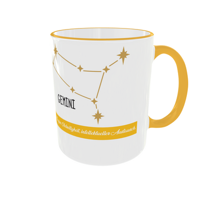 Weiße Keramiktasse mit gelbem Henkel und Rand, bedruckt mit dem Sternzeichen-Symbol „Zwillinge“ und dem Sternenbild „Gemini“ in Gold-Gelb.